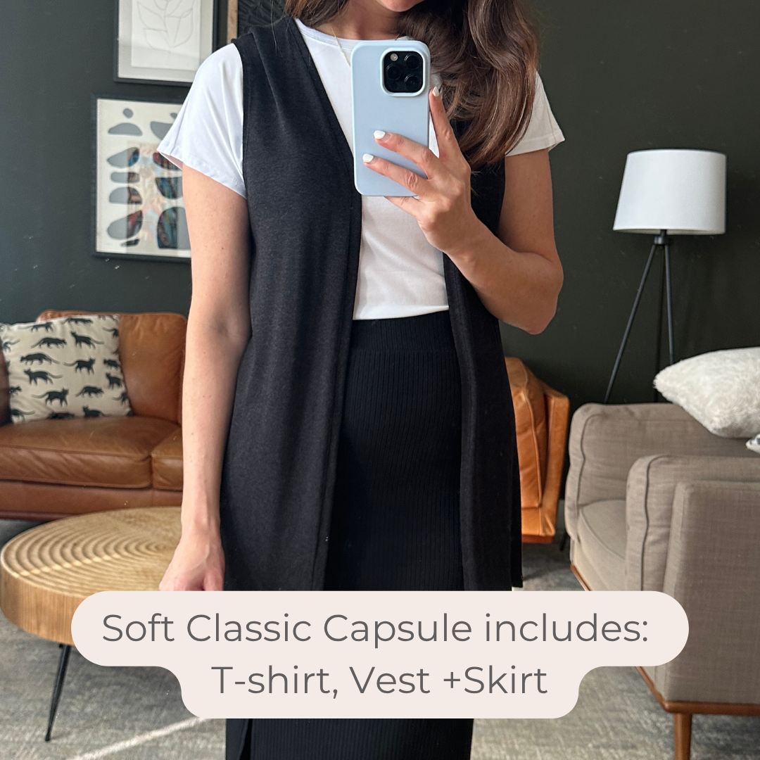 Woman taking a mirror selfie wearing a white t-shirt, black vest, and black skirt in a living room. Made in canada