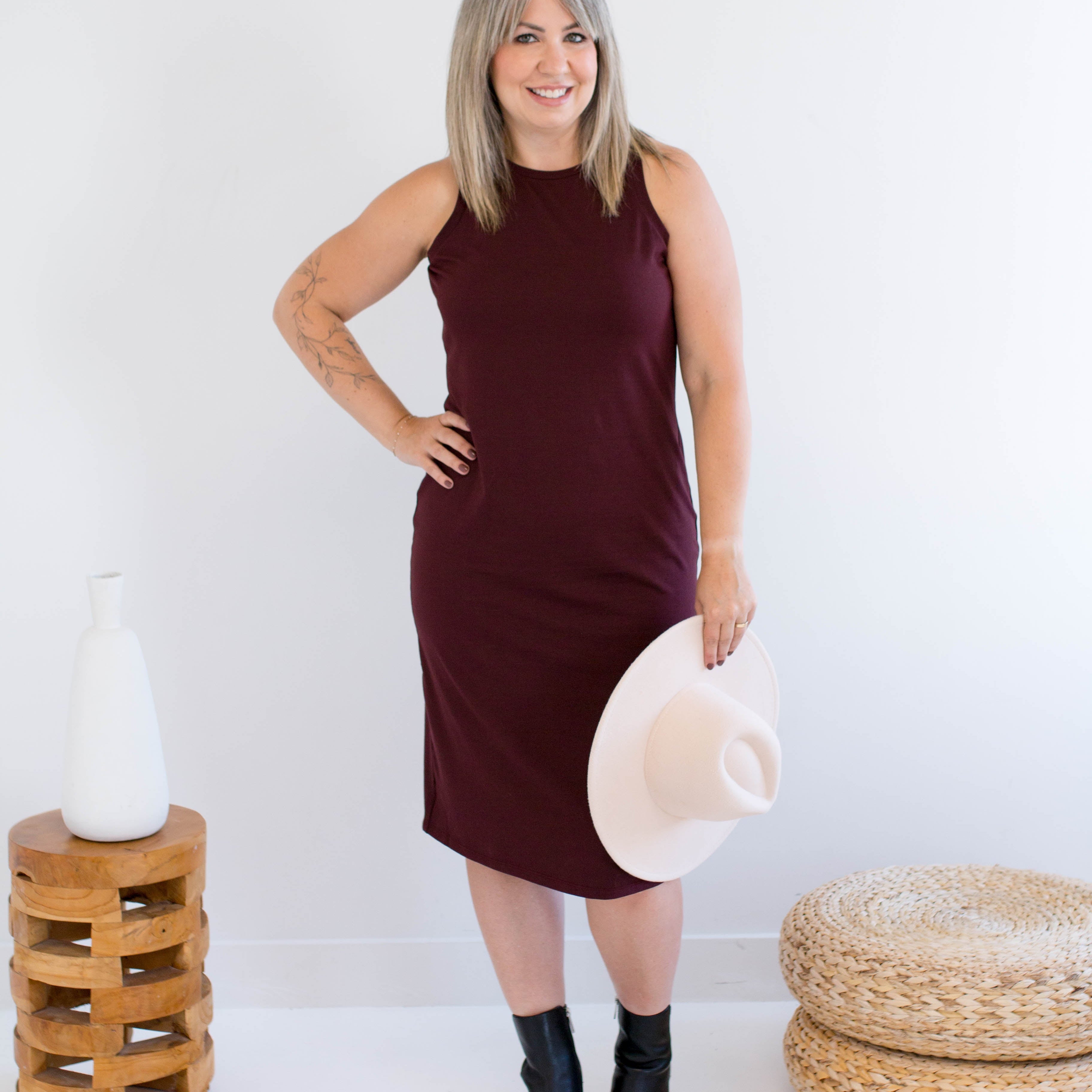 Woman in a burgundy tank dress made in canada holding a white hat against a white background