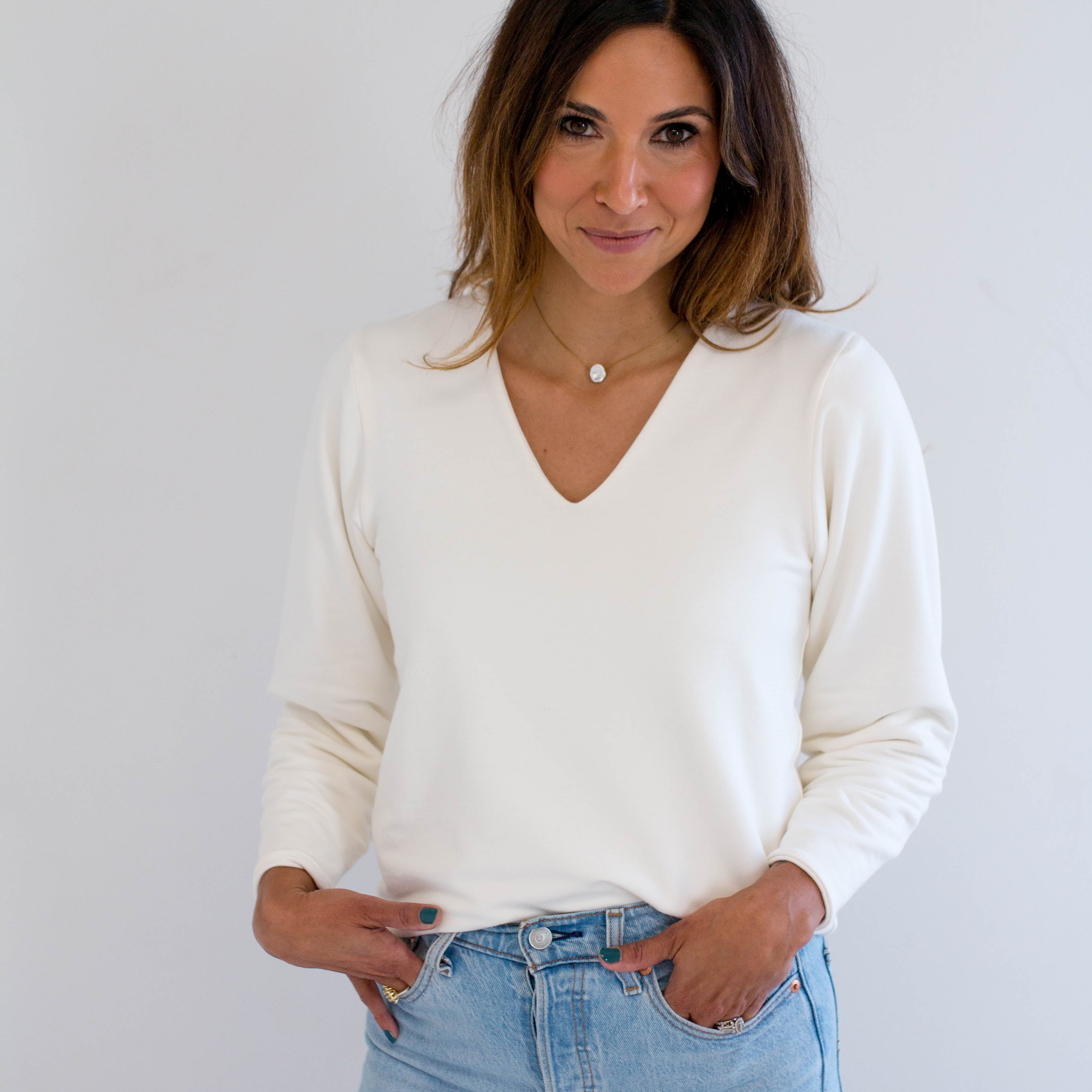 Woman wearing a cream bamboo v-neck sweater and light blue jeans against a plain background. made in canada clothing.