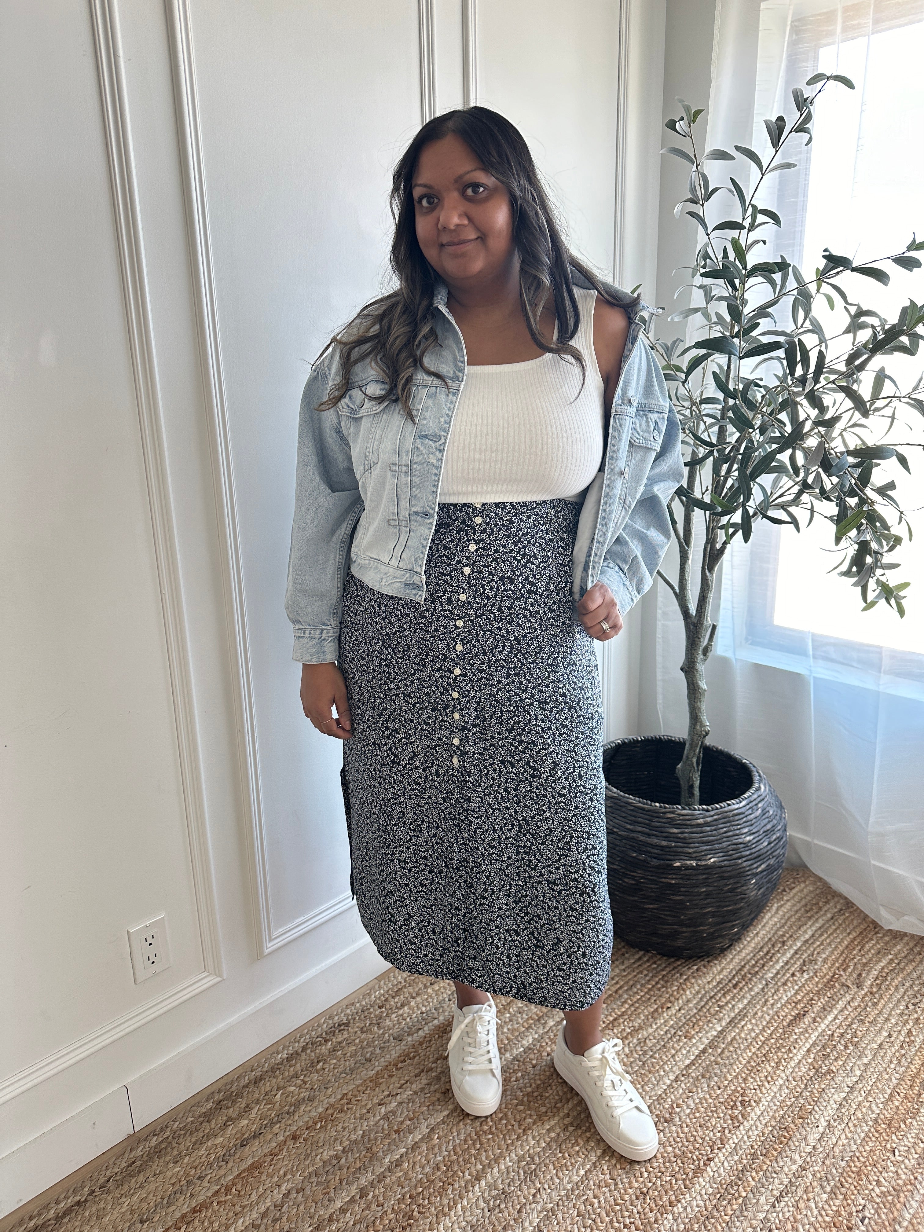 Indian woman wearing a denim jacket, white square neck tank top and black and white floral print midi skirt with buttons and side slits