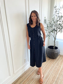 black loose fitting tank top with brown buttons and black loose fitting midi skirt with side slits with brown buttons on model standing wearing neutral sandals