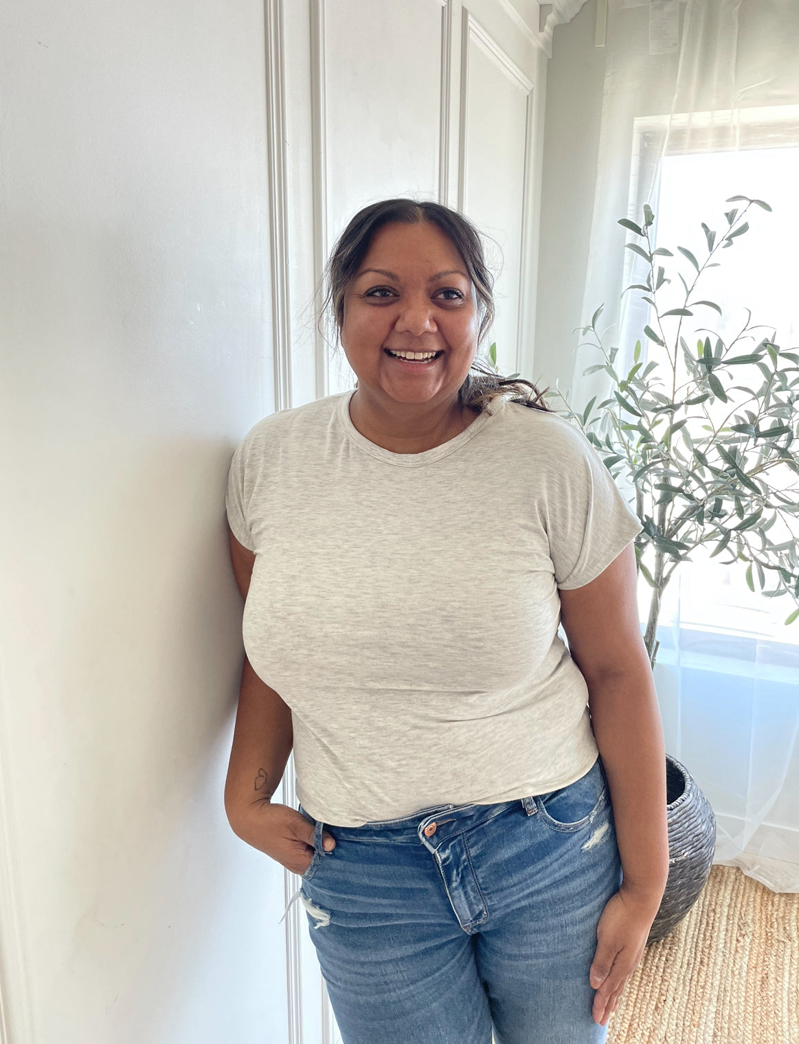 indian woman smiling wearing a light grey crewneck t-shirt and light wash jeans