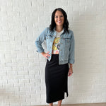 woman wearing jean jacket, graphic tee and black ribbed midi skirt with white sneakers