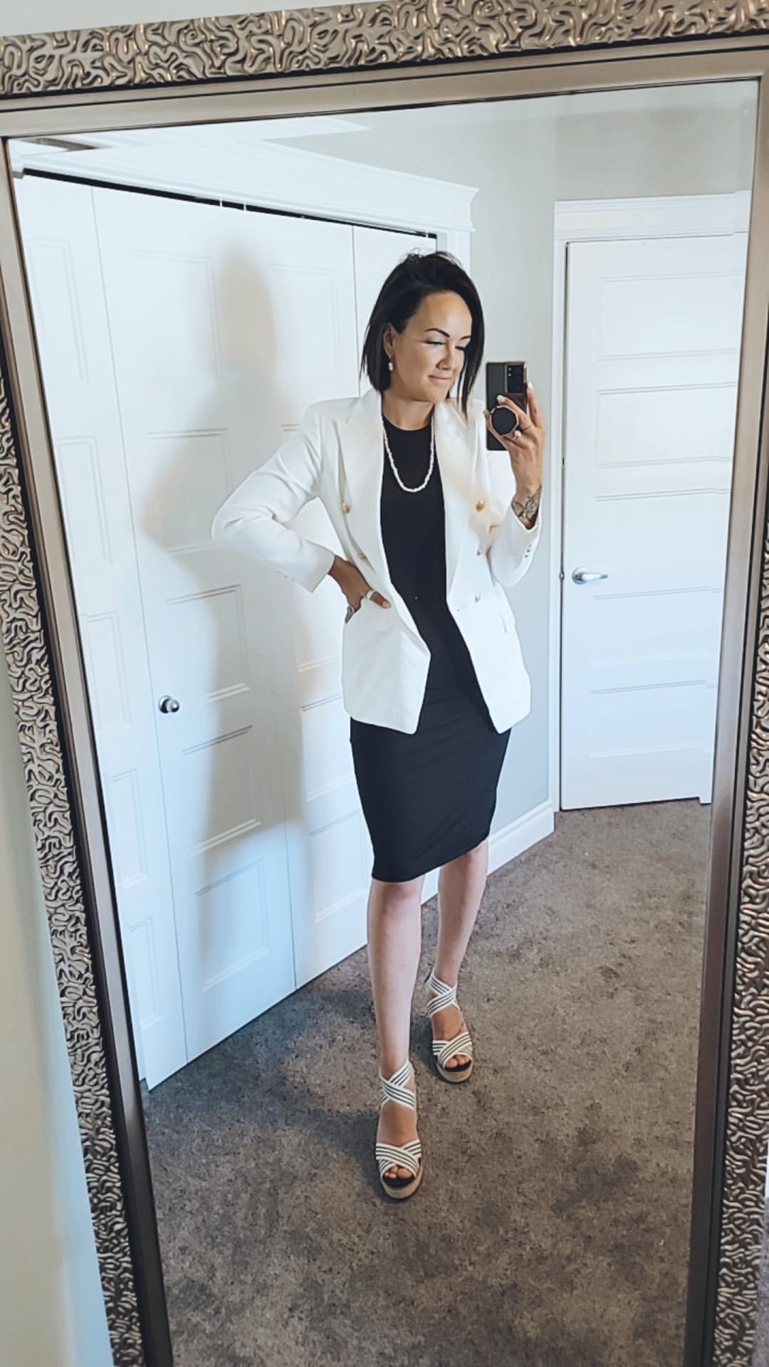 woman wearing black tank dress with a white blazer standing in mirror