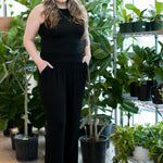 woman wearing a black tank top and black wide leg pants in front of plants