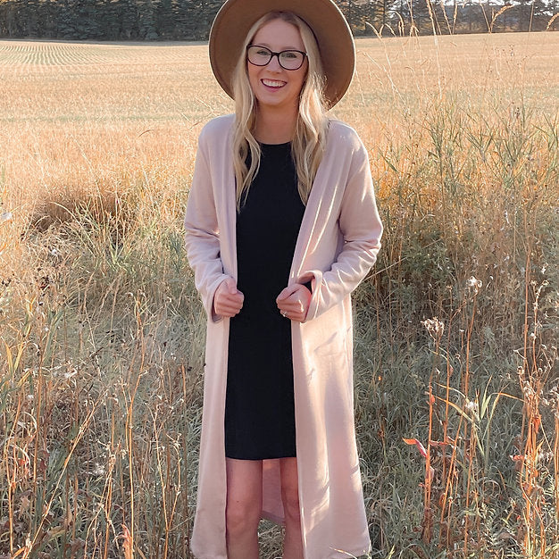 woman wearing long pink cardigan and black dress and hat