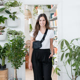 woman wearing a white vneck tshirt and black wide leg pants standing in front of a door with her hand in her pocket with a fanny pack 