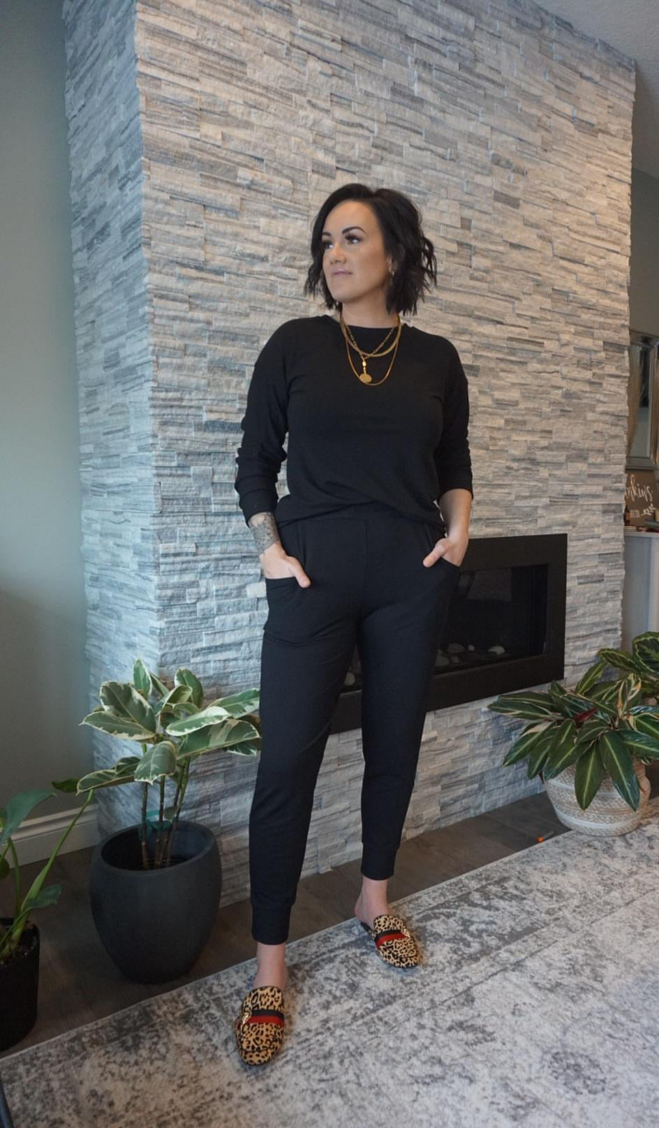 Model wearing black bamboo tapered joggers and black crewneck sweatshirt standing in front of fireplace