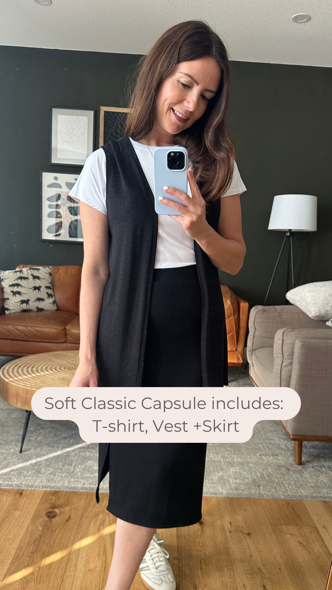 Woman taking a mirror selfie wearing a white t-shirt, black vest, and black skirt in a living room. Made in canada
