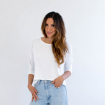 Woman wearing a white top and light blue jeans against a white background