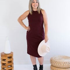 Woman in a burgundy tank dress made in canada holding a white hat against a white background
