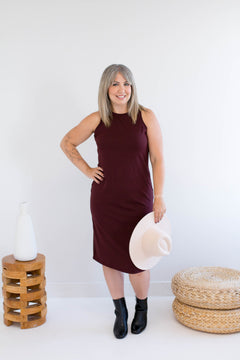 Woman in a burgundy tank dress made in canada holding a white hat against a white background