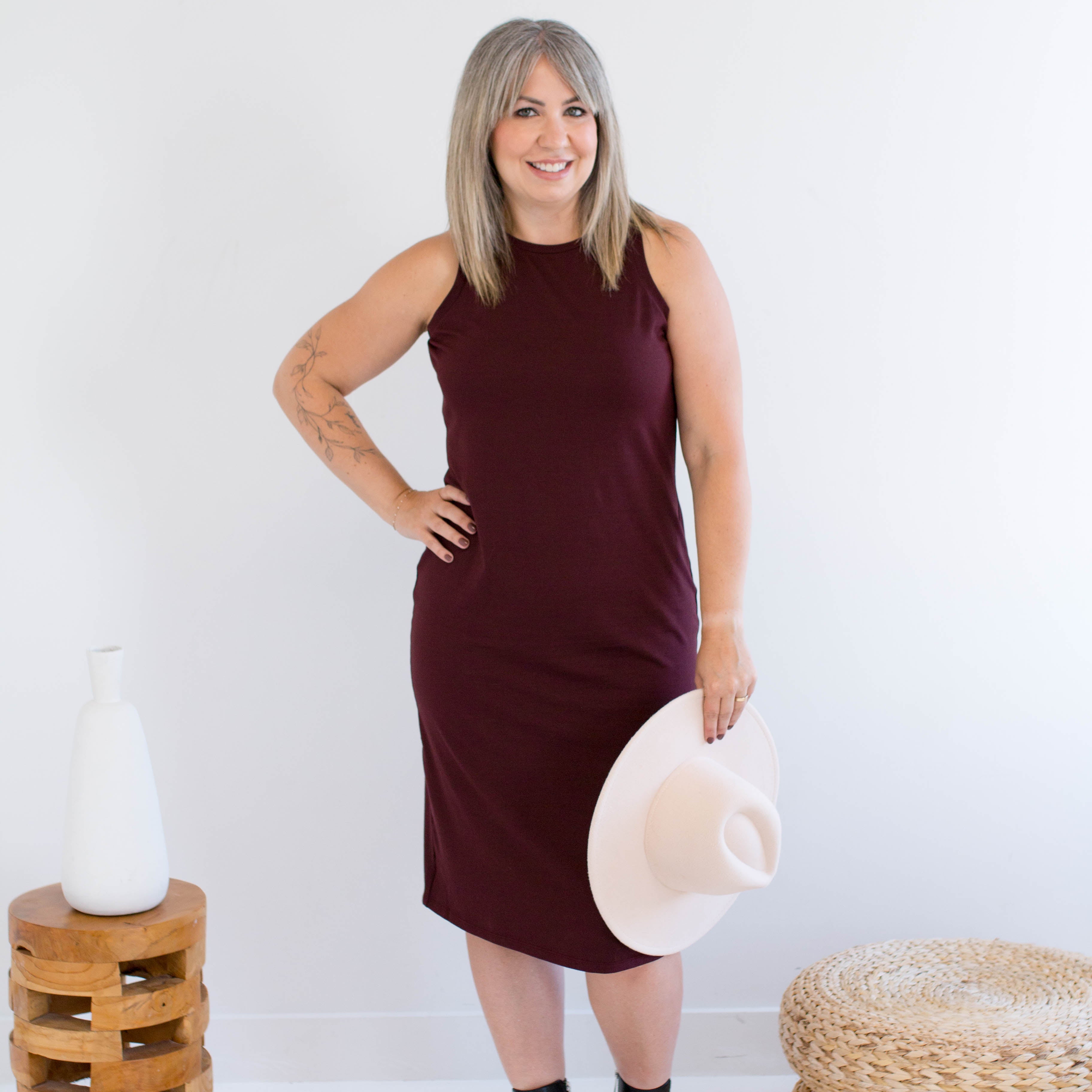 Woman in a burgundy tank dress made in canada holding a white hat against a white background