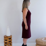 Woman wearing a burgundy tank dress made in canada standing in a minimalistic room with a white wall and wooden furniture.
