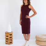Woman wearing a burgundy dress made in canada, white hat, and white boots standing against a white background.