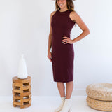 Woman wearing a burgundy dress made in canada, white hat, and white boots standing against a white background.