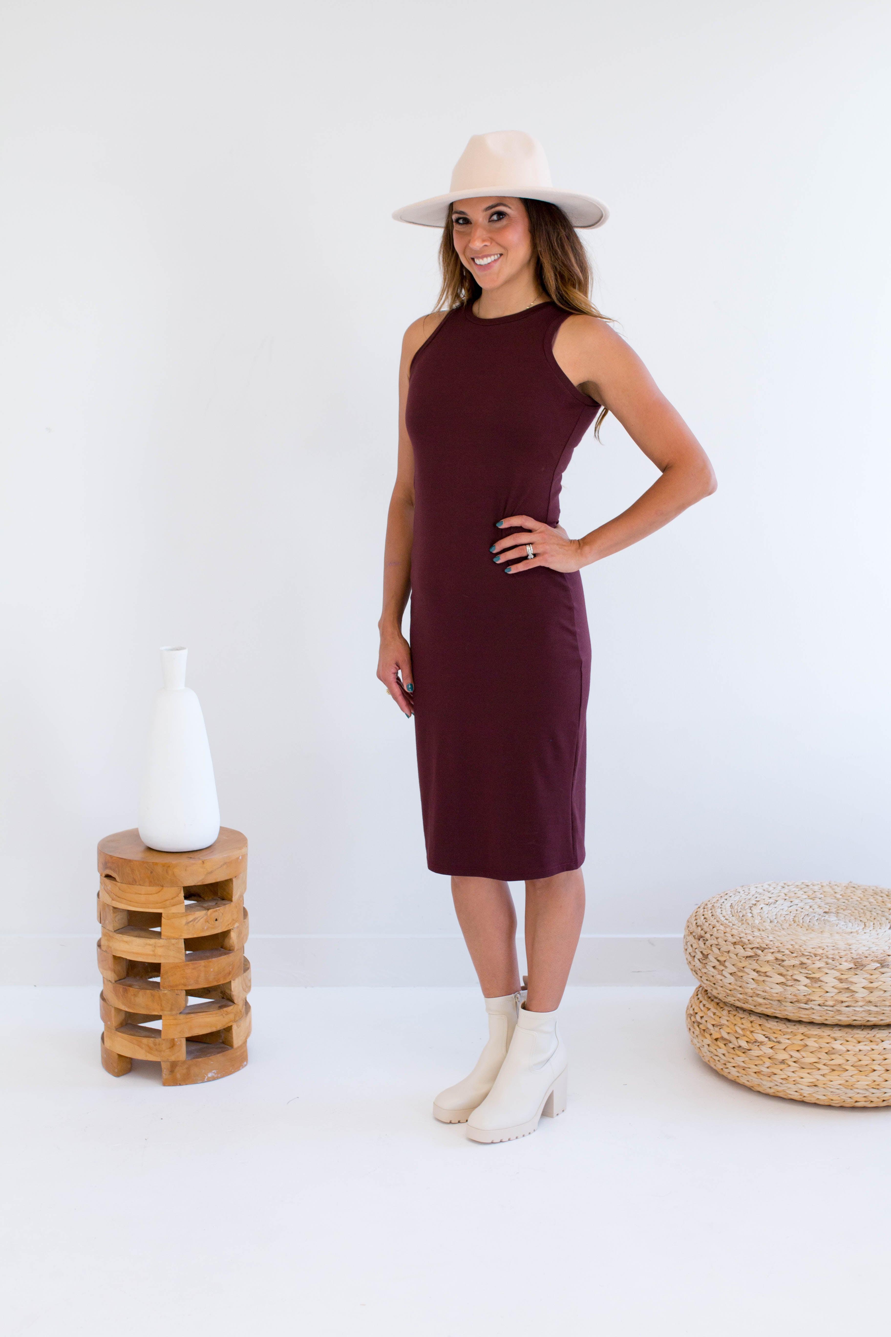 Woman wearing a burgundy dress made in canada, white hat, and white boots standing against a white background.