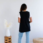 Woman wearing a black vest made in canada with light blue jeans in a minimalistic setting.