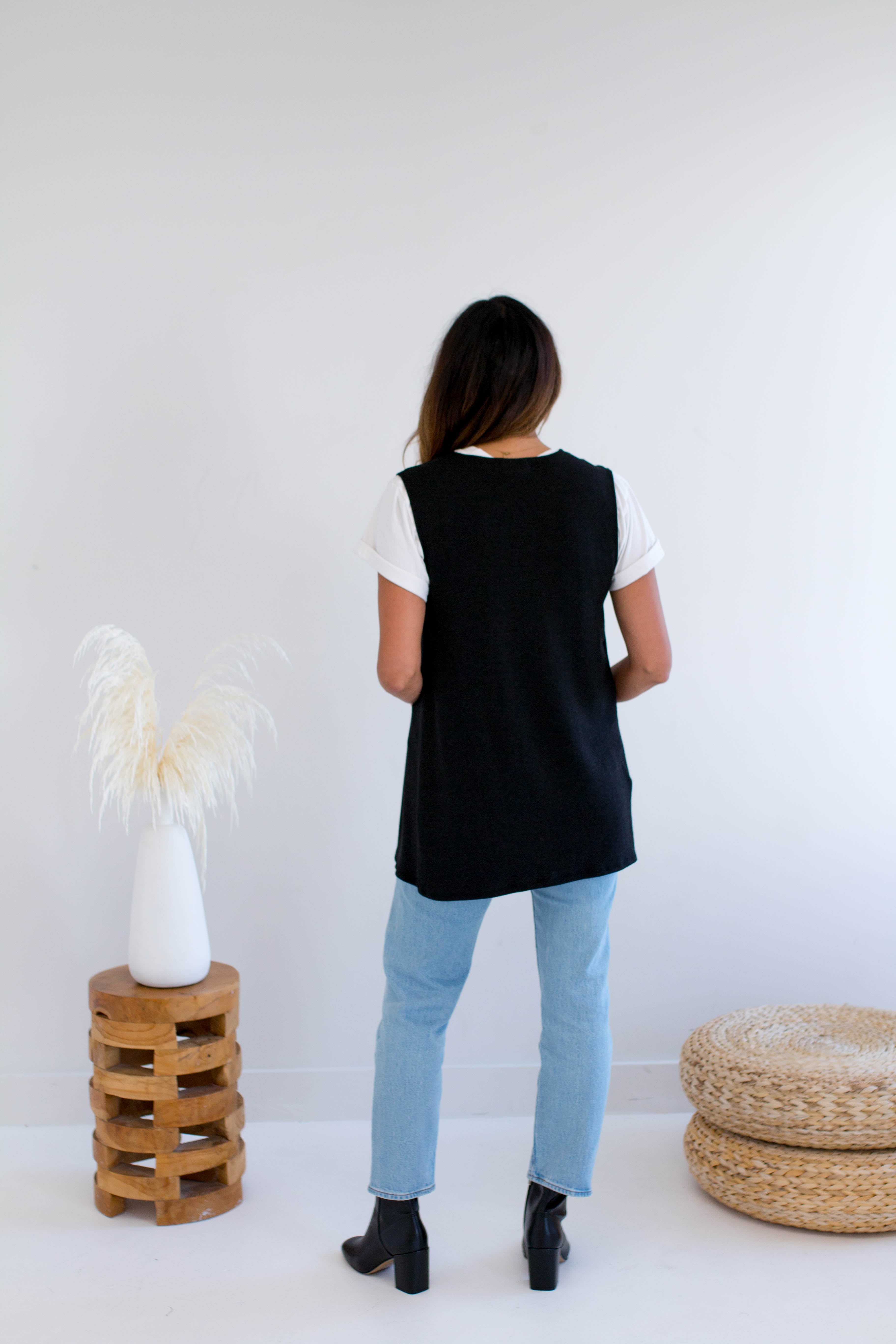 Woman wearing a black vest made in canada with light blue jeans in a minimalistic setting.