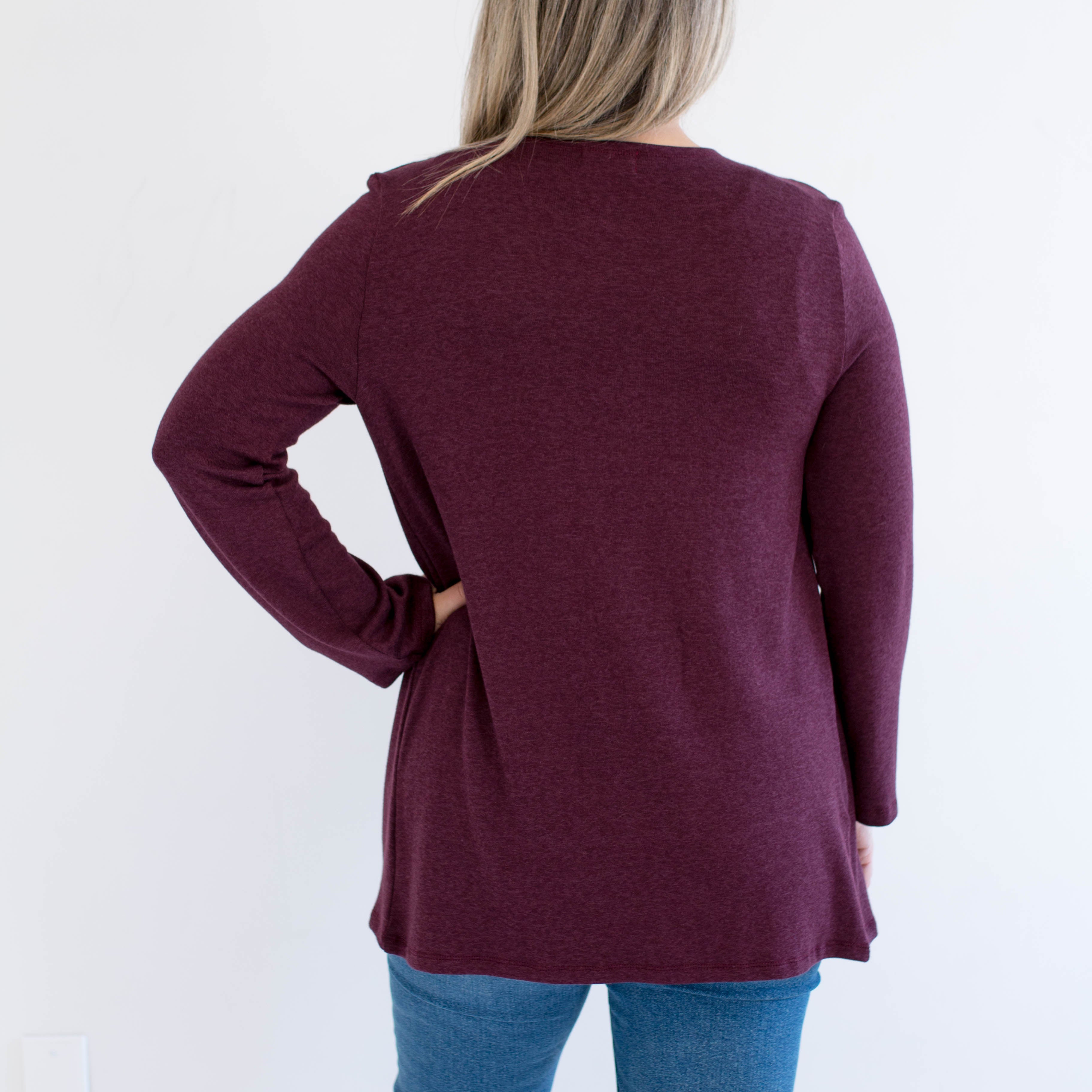 Person wearing a burgundy long-sleeve cardigan and blue jeans on a white background