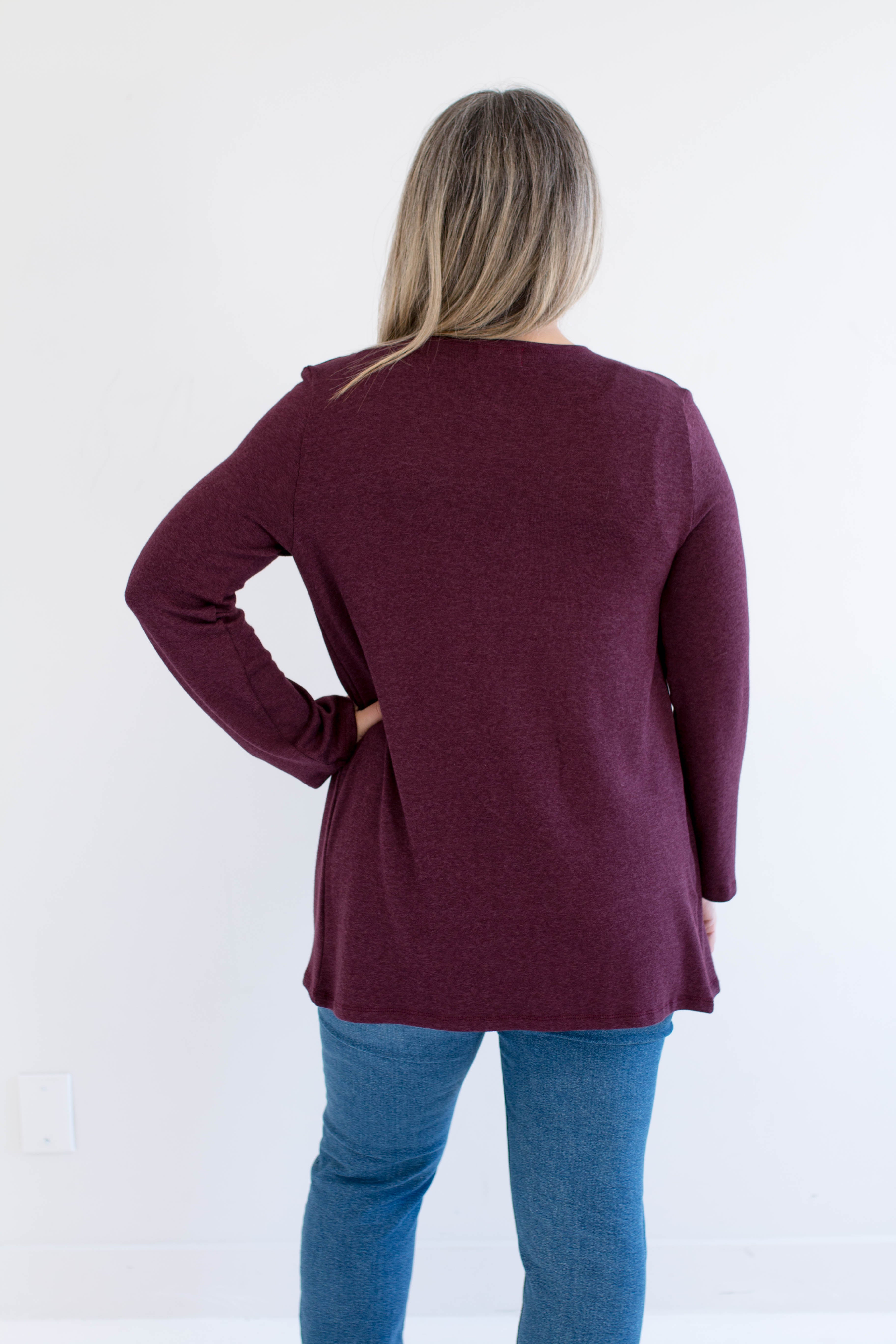Person wearing a burgundy long-sleeve cardigan and blue jeans on a white background