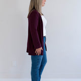Woman wearing a burgundy cardigan, white shirt, blue jeans, and black boots against a white background