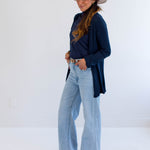 Woman wearing a navy cardigan made in canada, light blue jeans, and a beige hat on a white background