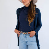 Woman wearing a navy cardigan made in canada, navy mockneck, light blue jeans, and a beige hat against a white background