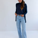 Woman wearing a navy sweater, light blue jeans, and a beige hat against a white background
