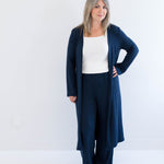 Woman wearing a navy blue cardigan and pants with a white top on a white background