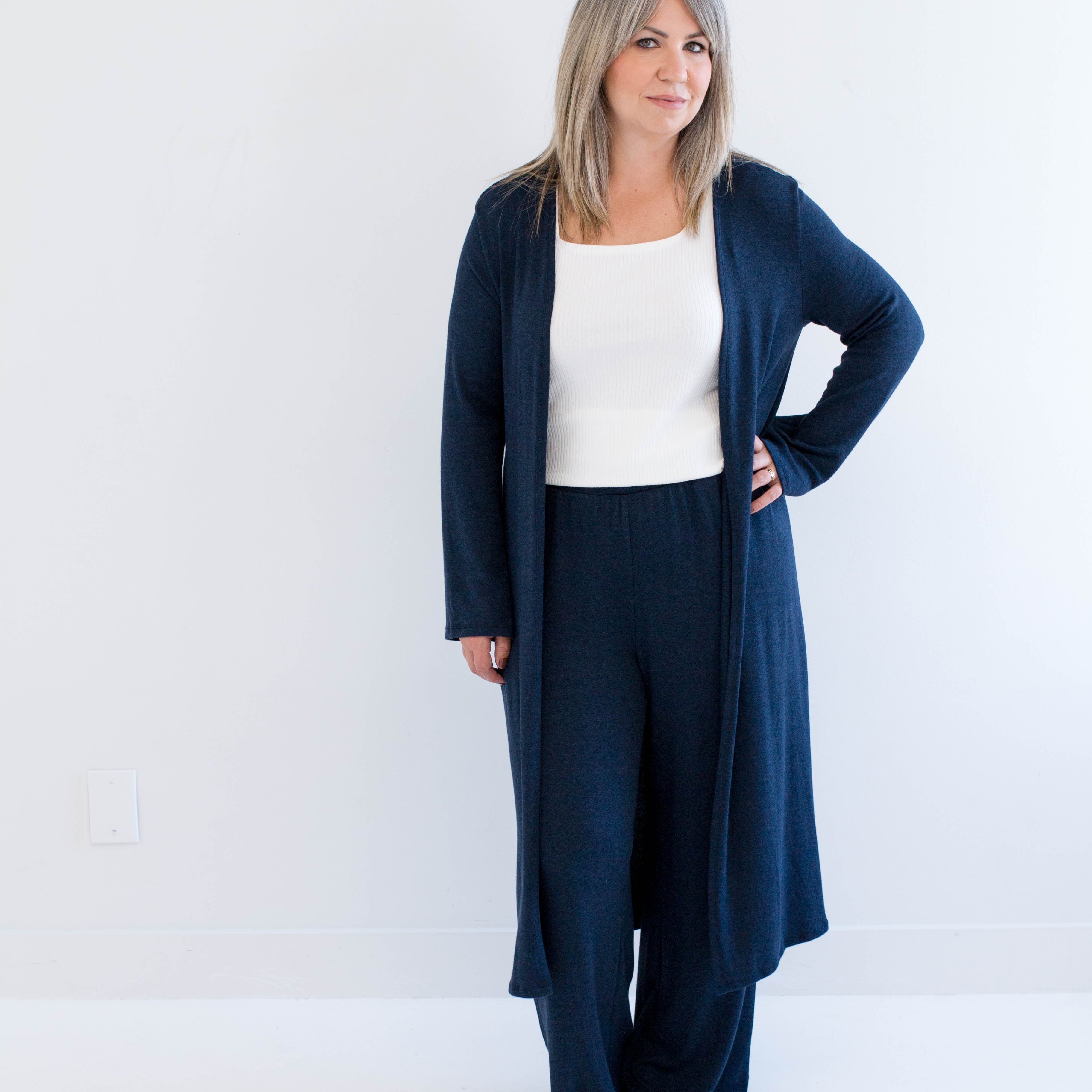 Woman wearing a navy blue cardigan and pants with a white top on a white background