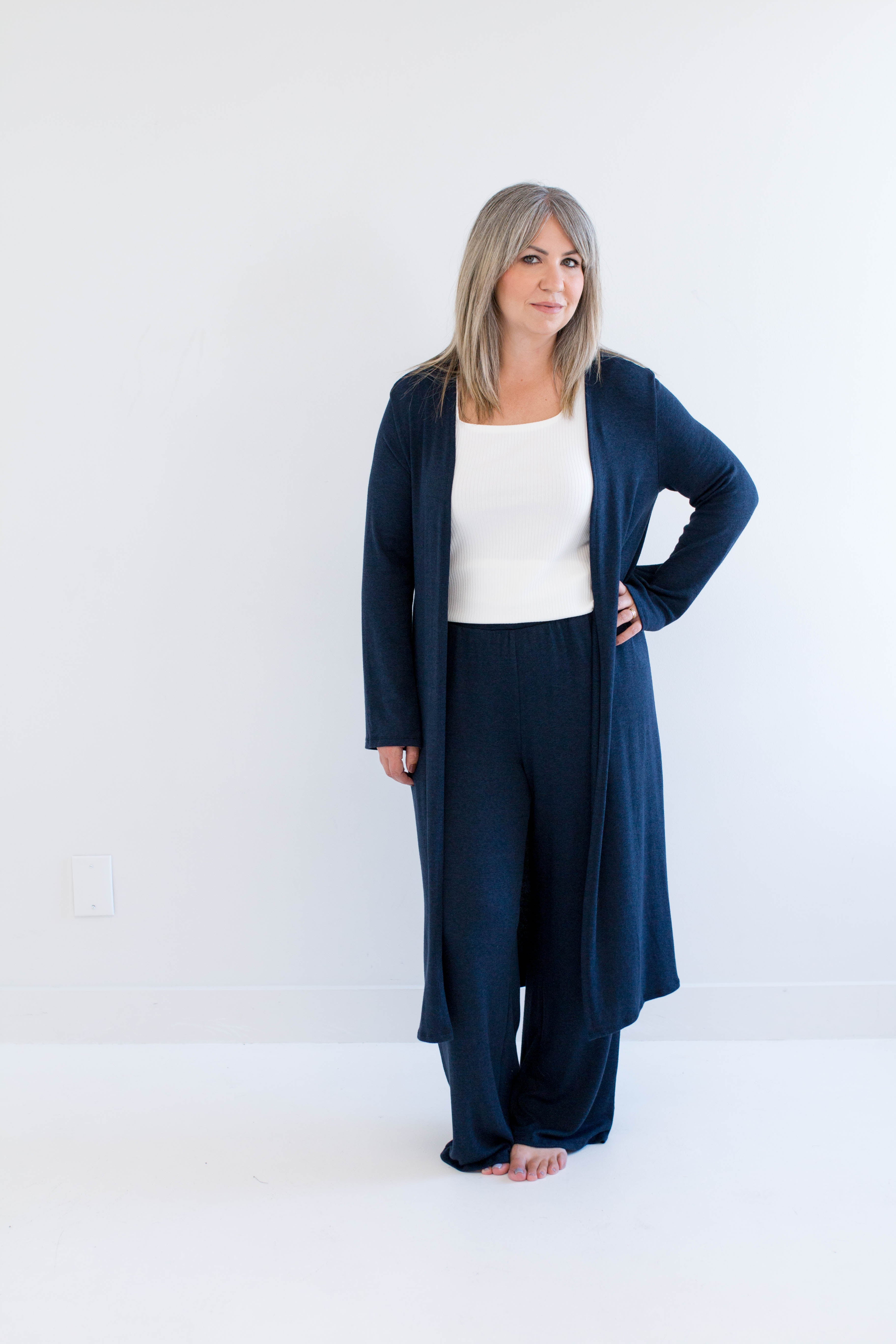 Woman wearing a navy blue cardigan and pants with a white top on a white background