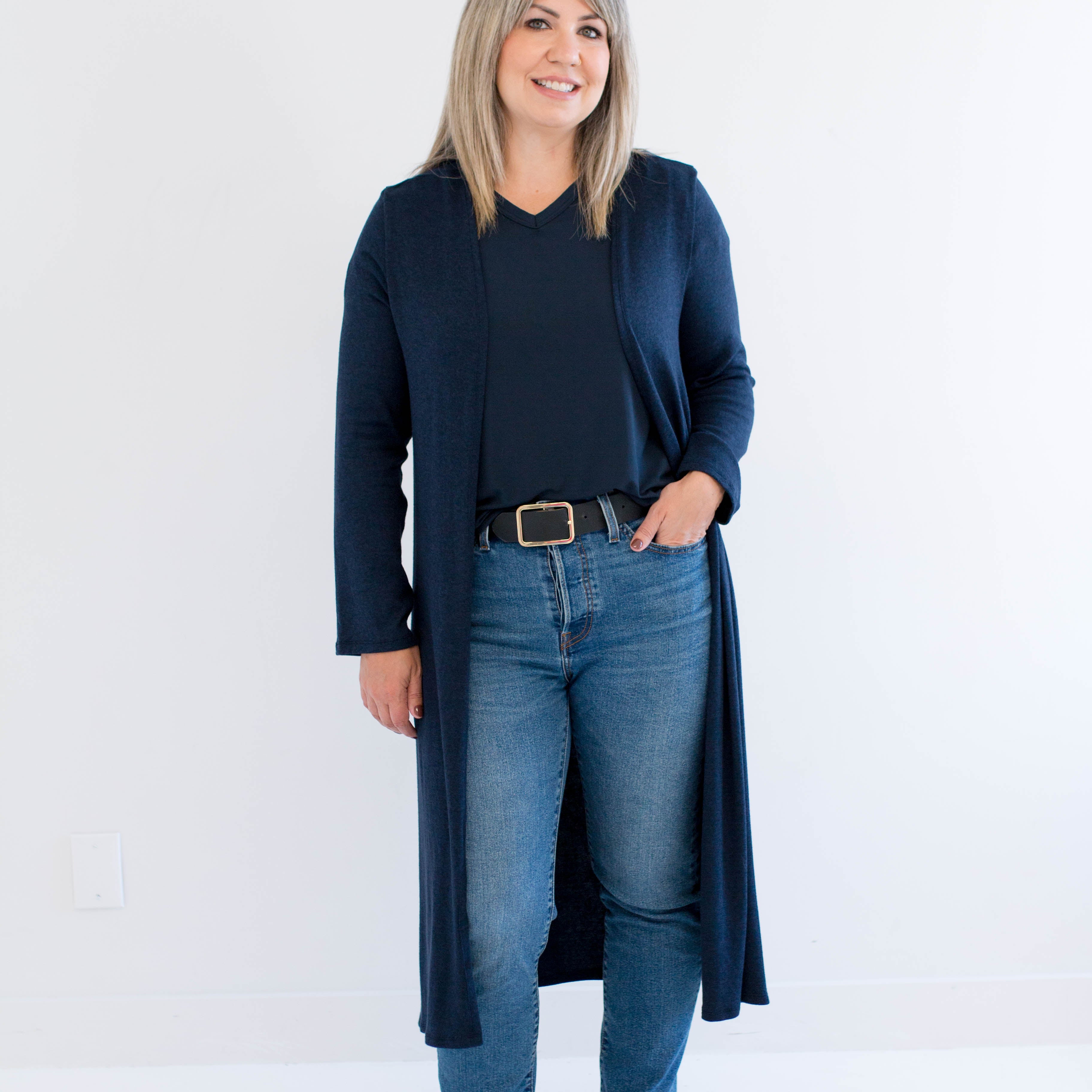 Woman wearing a long navy cardigan, black top, blue jeans, and black boots on a white background. Made in Canada.