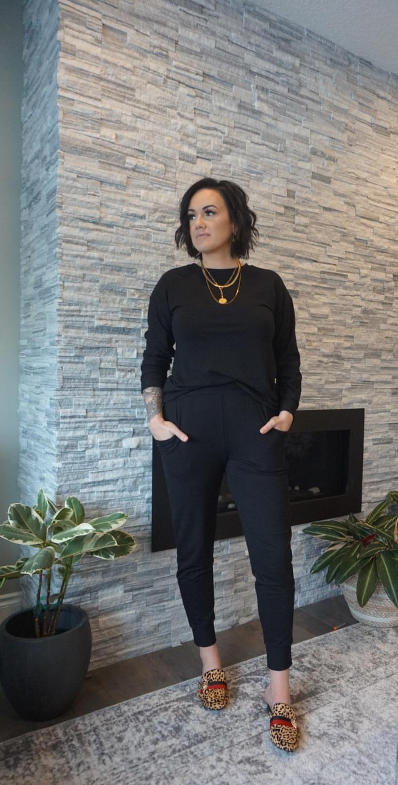 Model wearing black bamboo tapered joggers and black crewneck sweatshirt standing in front of fireplace