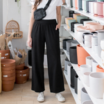 Woman standing in a pottery store with shelves of ceramic items wearing black wide leg bamboo pants made in canada