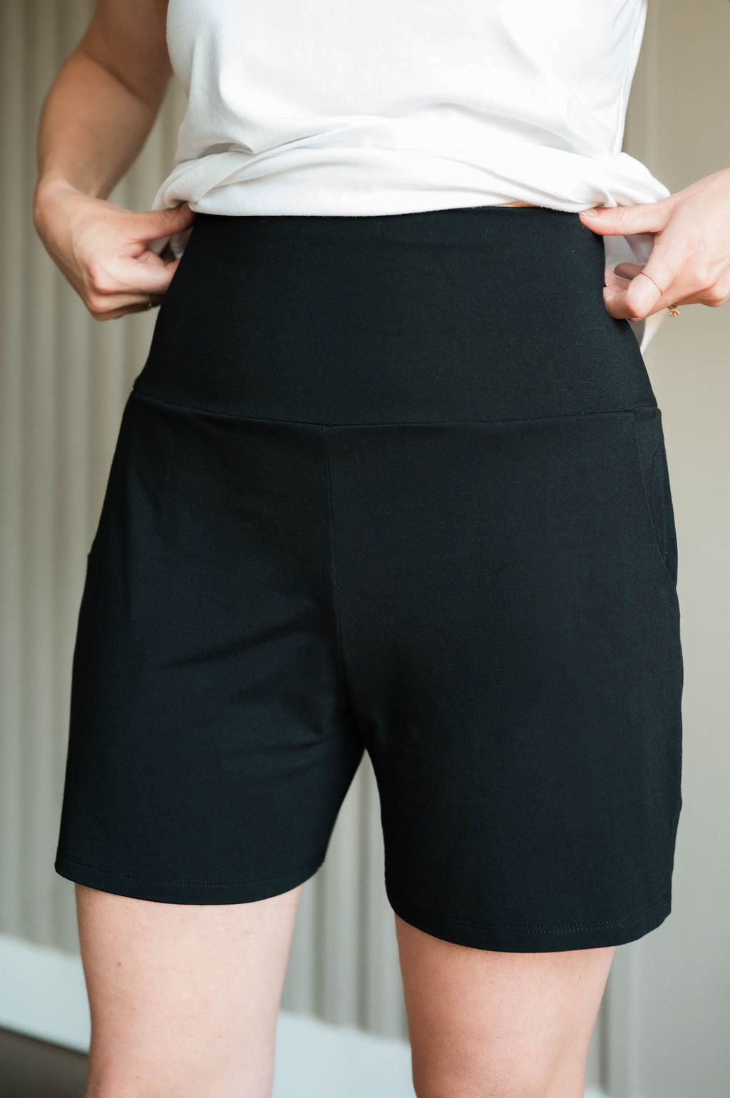 A close-up of a person wearing black high-waisted athletic shorts with a white top, showing the fit and side pockets. Made in Canada bamboo shorts.