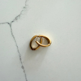 A pair of small gold huggie hoop earrings resting on a white marble surface.