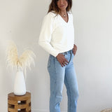 Woman wearing a off-white sweater and light blue jeans standing in a minimalistic room.