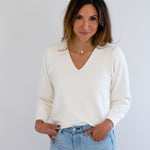 Woman wearing a cream bamboo v-neck sweater and light blue jeans against a plain background. made in canada clothing.