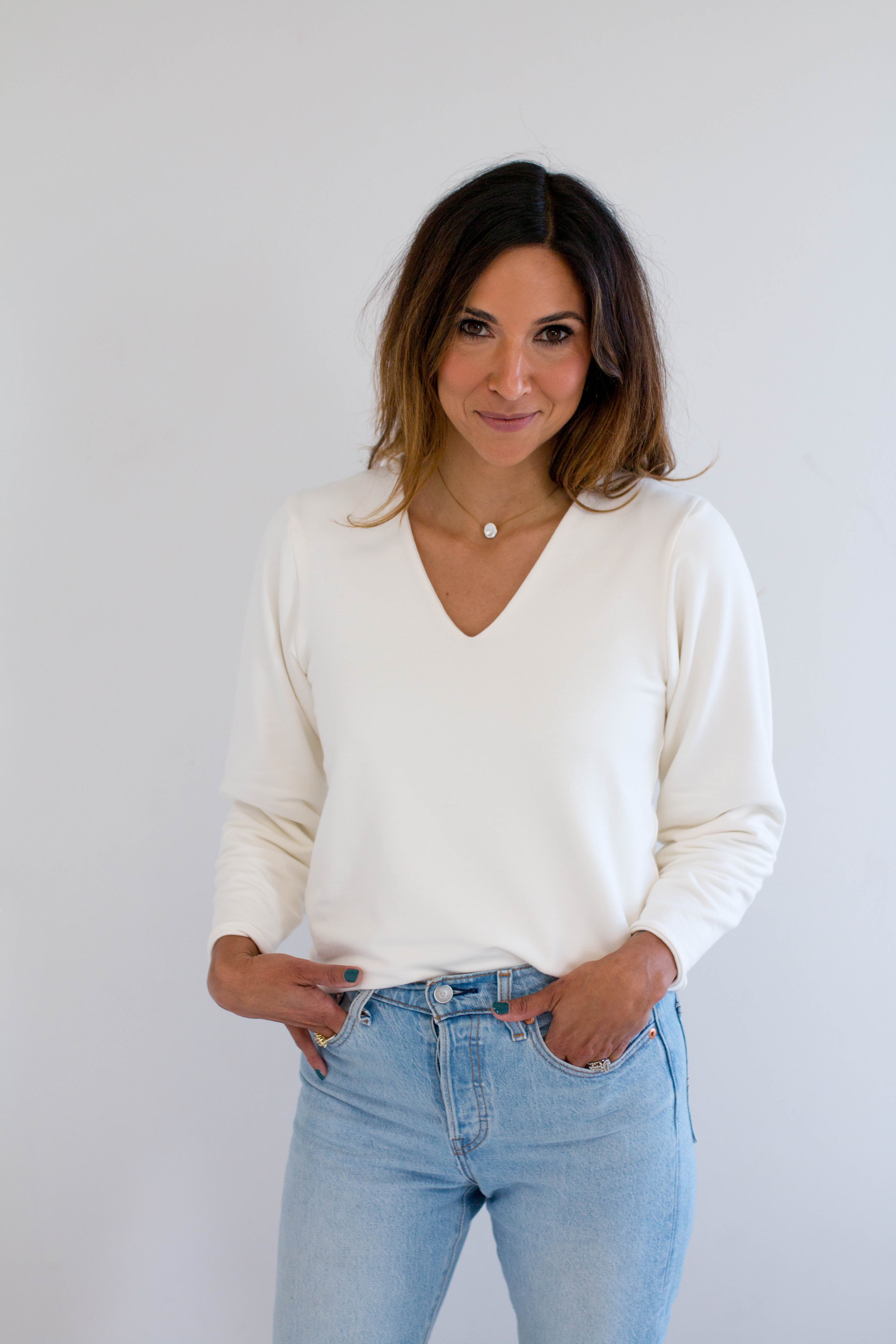 Woman wearing a cream bamboo v-neck sweater and light blue jeans against a plain background. made in canada clothing.