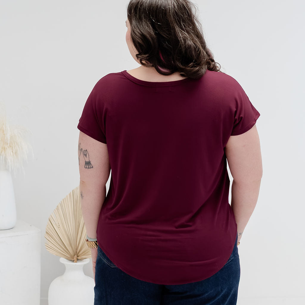 A woman viewed from behind wearing a short-sleeve crewneck t-shirt in burgundy and dark blue jeans, standing in a bright, minimalist room with white walls and decorative vases.  bamboo clothing made in canada