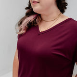 A woman wearing a short-sleeve V-neck t-shirt in deep burgundy, shown from the chest up against a light gray studio background.