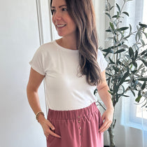 Woman standing in a room with white walls and a plant in the corner wearing a white bamboo t-shirt made in canada
