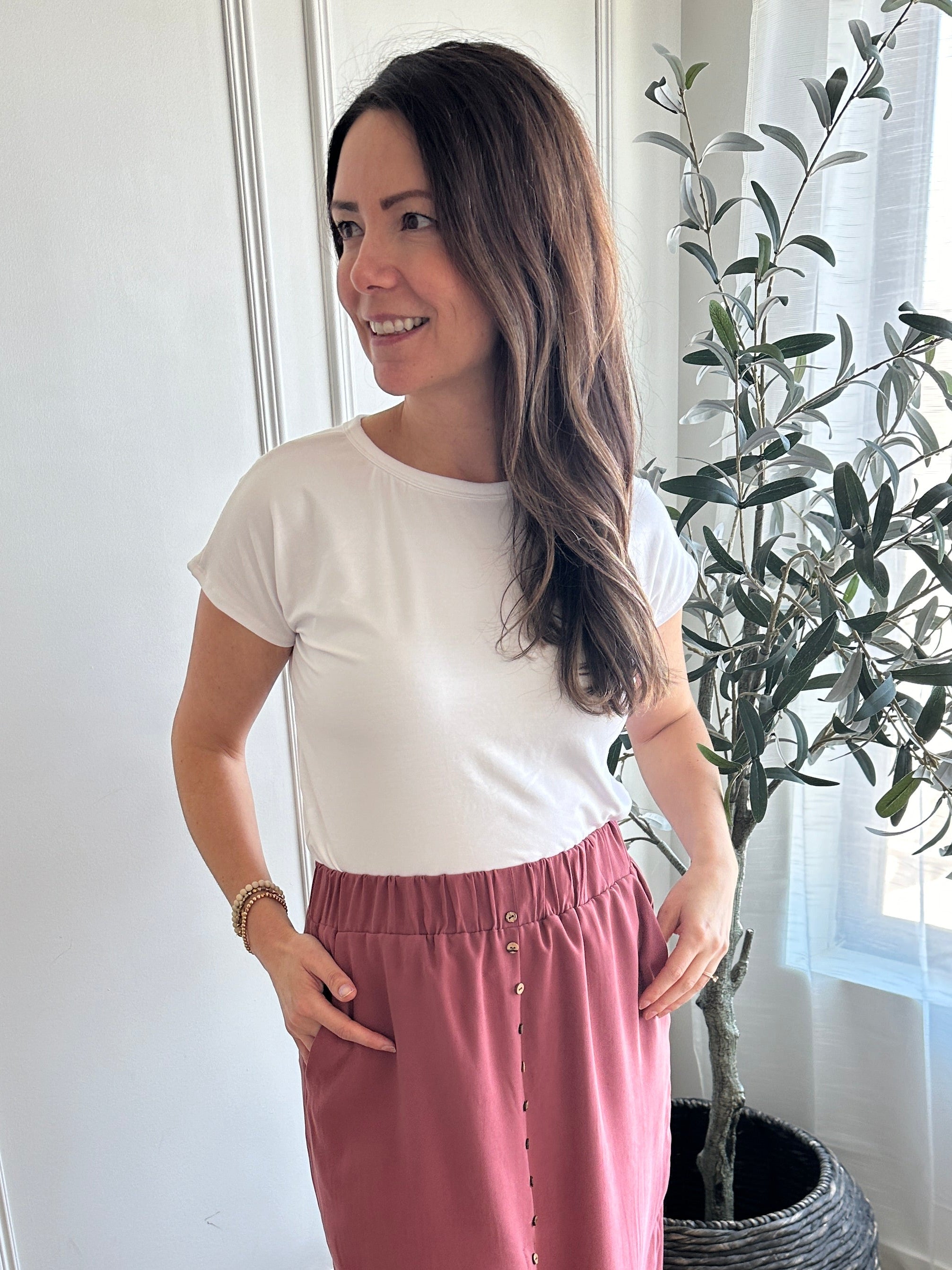 Woman standing in a room with white walls and a plant in the corner wearing a white bamboo t-shirt made in canada