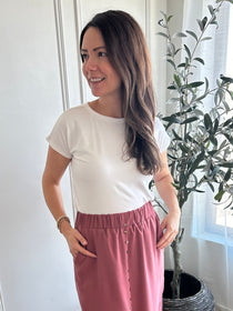 Woman standing in a room with white walls and a plant in the corner wearing a white bamboo t-shirt made in canada