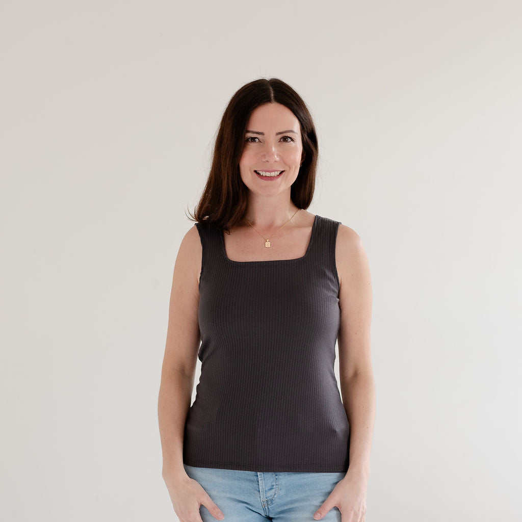 Woman wearing a grey tank top and light blue jeans against a plain background