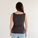 Woman wearing a dark gray tank top and light blue jeans against a white background. made in canada back view of tank.
