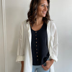 black loose fitting tank top with brown buttons with white button-up shirt over top. paired with denim.