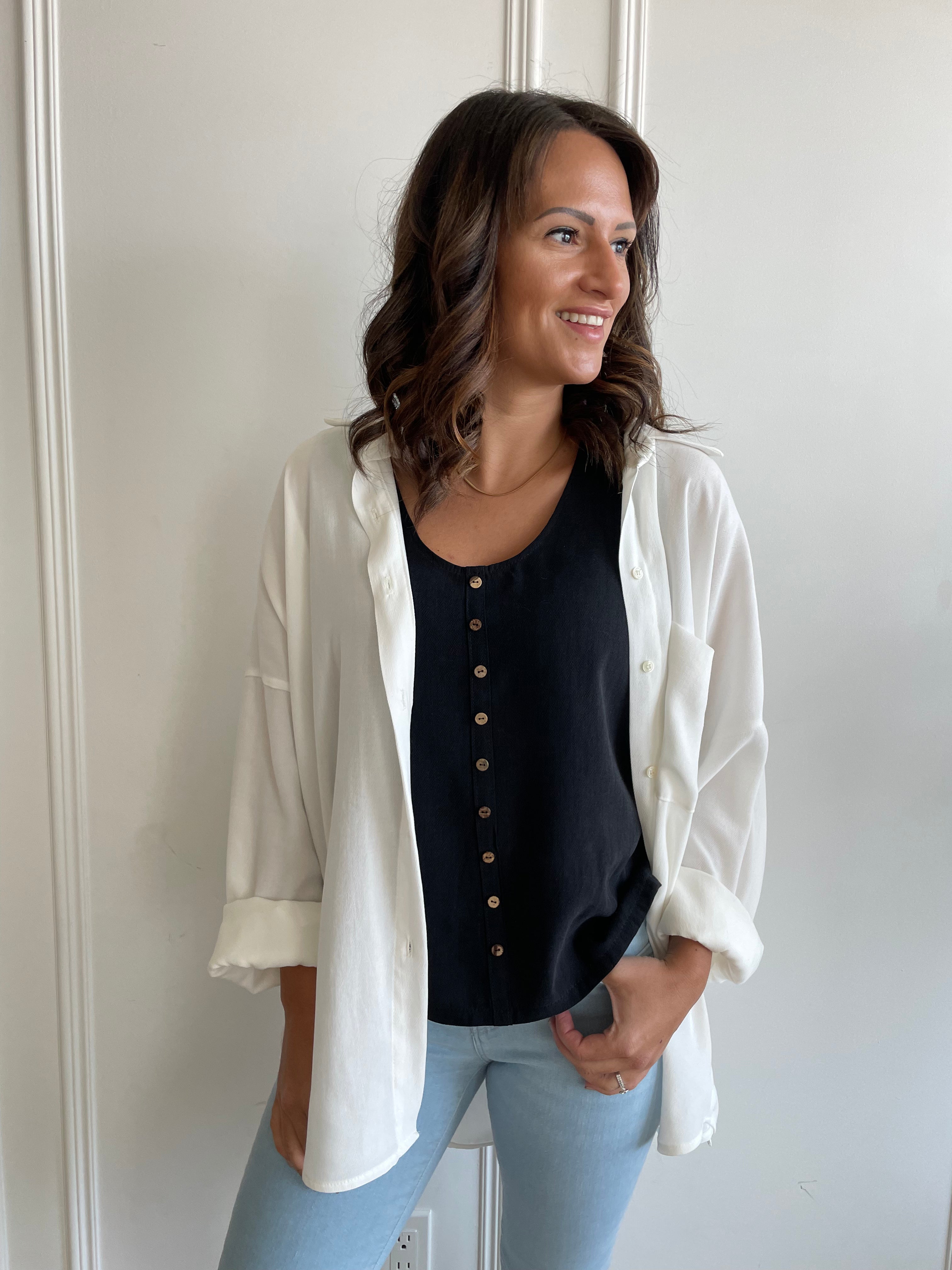 black loose fitting tank top with brown buttons with white button-up shirt over top. paired with denim.