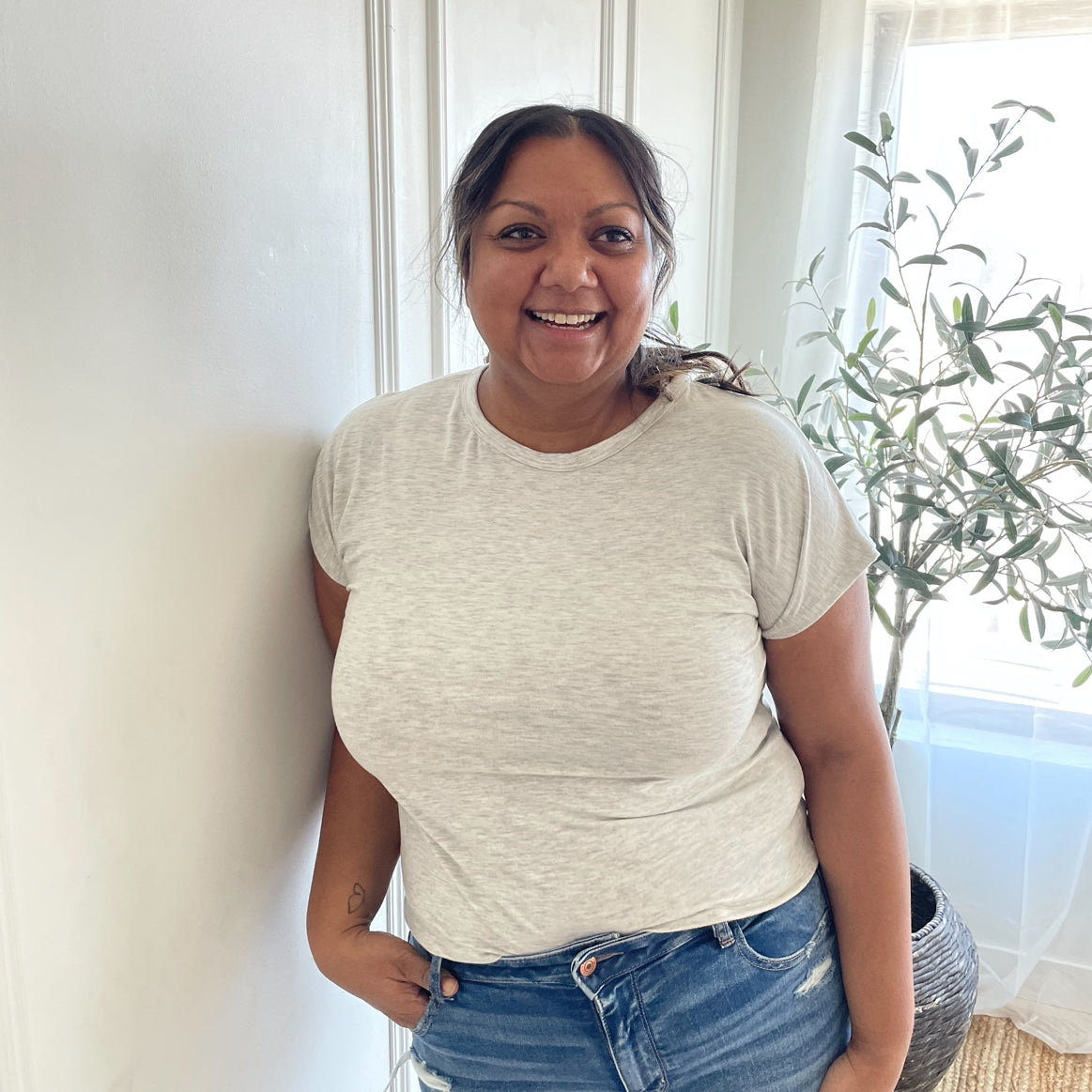indian woman smiling wearing a light grey crewneck t-shirt and light wash jeans